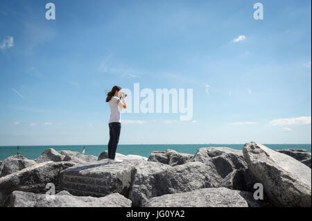 woman with a camera on top of rocks by the coast taking photographs