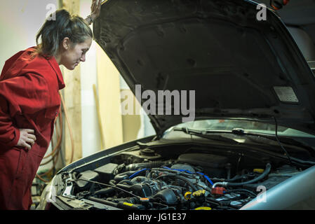 Female mechanic inspecting car engine with hand on hood Stock