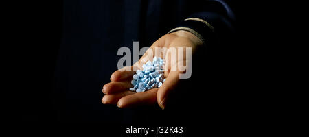 Black Mania. female hand isolated on black showing blue pills Stock Photo