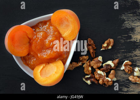 Apricot jam and walnuts arranged on black wooden background Stock Photo