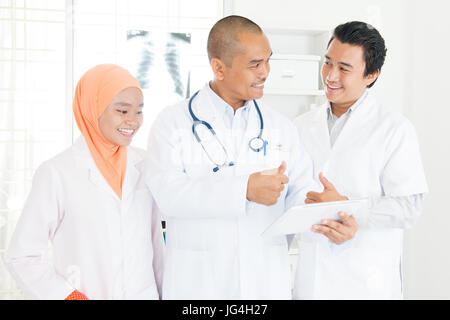 Medical team discussing over digital tablet in hospital and giving thumb up. Southeast Asian Muslim doctors. Stock Photo