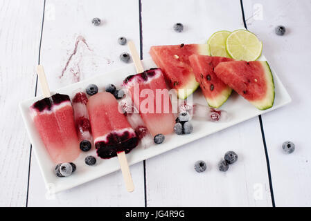 Popsicles with watermelon, coconut milk, lime, raspberries and blueberries. Popsicle on a white rectangular plateau, rectangle ice with raspberries. L Stock Photo