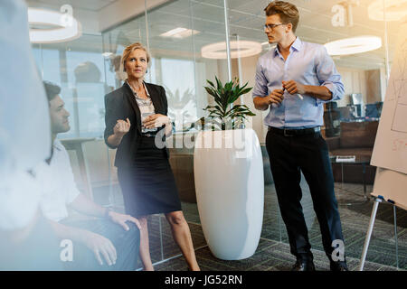 Mature businesswoman discussing with colleagues during presentation in modern office. Business people having a brainstorming meeting in office. Stock Photo