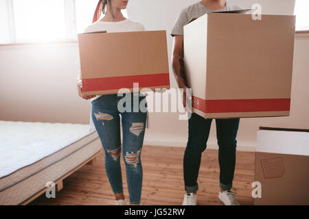 Young couple with big cardboard boxes moving to new place. Cropped shot of man and woman carrying big boxes and moving into new house.
