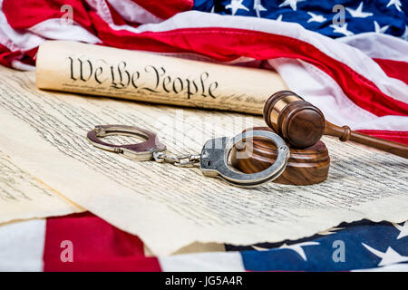 The United States Constitution rolled up on an American flag with a gavel and handcuffs in the foreground. Stock Photo