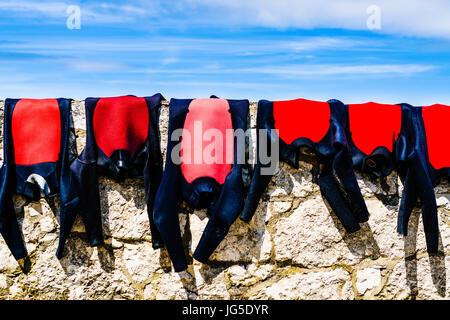 Wetsuits drying on a coastal stone wall. Stock Photo