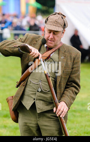 A man dressed in green Irish Lovat tweed jacket, deerstalker hat, waistcoat and trousers, loads his flintlock rifle with gunpowder. Stock Photo