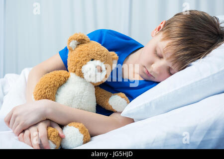 Sick little boy sleeping in hospital bed with teddy bear Stock Photo