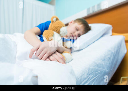 Sick little boy sleeping in hospital bed with teddy bear Stock Photo