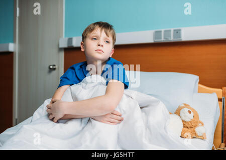 portrait of little thoughtful boy sitting on hospital bed Stock Photo
