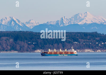 Log ship used for logging passes through Puget Sound, Washington with Cascade Mountains in background. Stock Photo