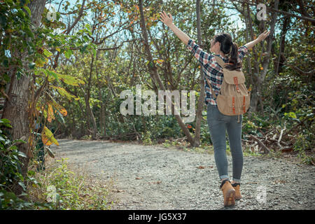 attractive young tourist backpacker walking in national park and opening hands enjoying nature atmosphere at summer vacation with back view photo. Stock Photo