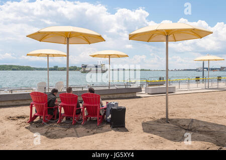 Toronto, Canada - 26 June 2017: Three men sitting next to travel backs on Toronto Beach and looking at Ontario Lake Stock Photo