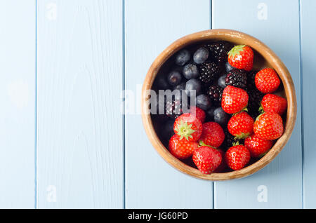 A shabby old wooden bowl of Summer berry fruits shot from above, on a freshly painted pale blue wood planked table. Stock Photo