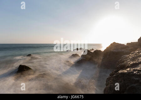 Motion blur waves breaking over rocks with setting sun at Pirates Cove in Malibu, California. Stock Photo