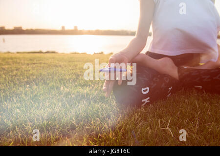 A teenager girl in lotus pose with spinners. Girl with a Tri Fidget Hand Spinner on her hand outdoors. Green grass in the background. Stock Photo