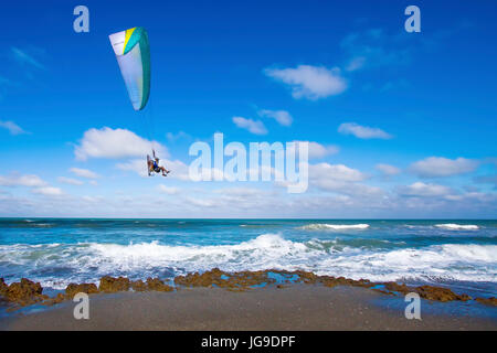 A motorized paraglider sails over the crashing waves of the Atlantic Ocean on a Florida Beach. Stock Photo