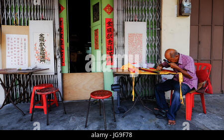 A Chinese man writes Chinese script outside his calligraphy business in Georgetown, Penang, Malaysia Stock Photo