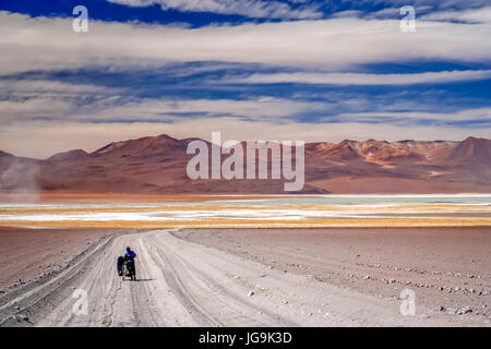 Woman cyclist struggling and pushing her bike on the sandy corrugated road in Altiplano in Bolivia Stock Photo