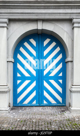 Old wooden door with white and blue stripes pattern in gray stone wall, background texture. Luzern, Switzerland Stock Photo