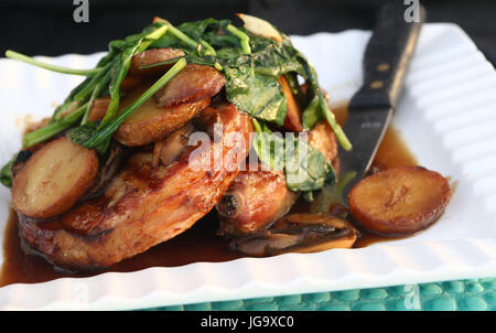 Wilted spinach over pork chops with mushroom gravy and roasted potatoes on white ridged dish with knife Stock Photo