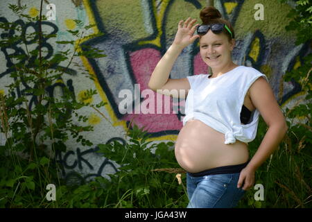Happy young  pregnant teenage woman with sunglasses looking cheeky into the camera Stock Photo