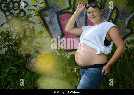 Happy young  pregnant teenage woman with sunglasses looking cheeky into the camera Stock Photo