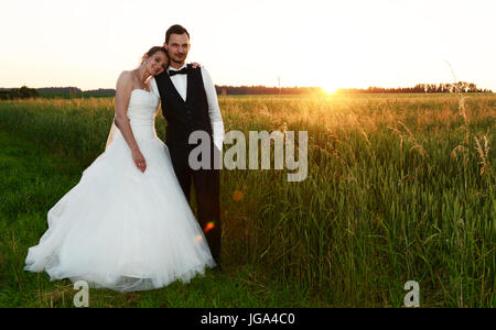 happy fresh married couple, looking into the camera and standing in a field while sunset Stock Photo