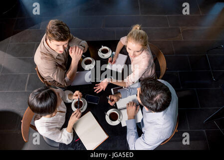 Overhead view of young businesspeople discussing project at table with cups of coffee, business lunch concept