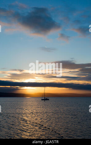 Sailboat with fallen sails in sunrise light on full North Sea in Weymouth Bay at Weymouth coast. Vertical composition with sailboat in center on low h Stock Photo