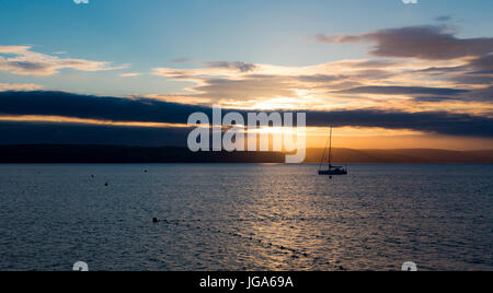 Sailboat with fallen sails in sunrise light on full North Sea in Weymouth Bay at Weymouth coast. Horizontal composition with sailboat in center and lo Stock Photo