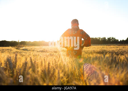 African woman in traditional clothes standing in a field of barley or wheat crops at sunset or sunrise Stock Photo