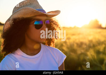 Beautiful happy mixed race African American female girl teenager young woman wearing relective aviator sunglasses and cowboy hat in a cornfield at gol Stock Photo