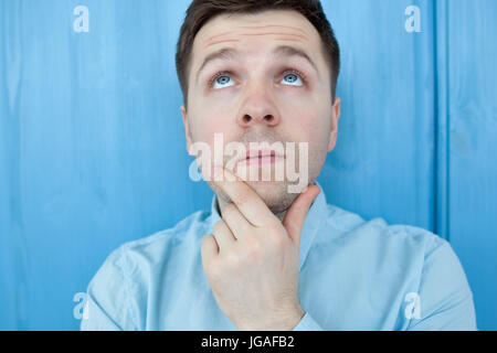 Caucasian thoughtful young man standing by the blue woodenwall. Stock Photo