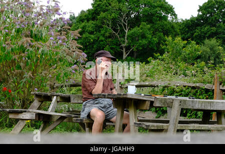 Sussex, UK. Solitary elderly make hiker talking on his mobile phone whilst seated at picnic table. Stock Photo