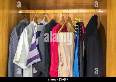 An open pine wood wardrobe containing a variety of mens' casual clothes on hangers, hanging from a rail. England, UK. Stock Photo