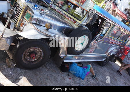 Broken down silver decorated Jeepney being repaired by man on sunny day.  A converted Jeep this is a common public transport in Philippines,  Baguio. Stock Photo