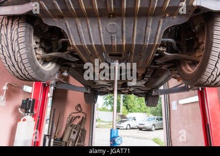 Big black car on a lift in a small empty auto service station Stock Photo