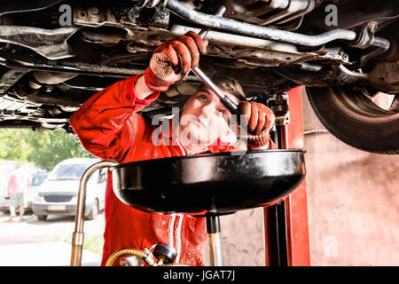 Male mechanic hooking up equipment to the undercarriage of a car elevated on a hoist during repairs and maintenance in a garage workshop Stock Photo