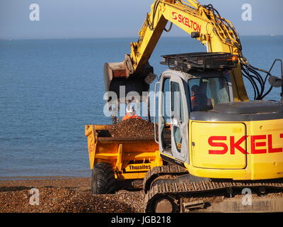 Close up of a small excavator loading shingle into a dumper truck on a beach. Stock Photo