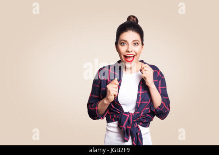 Portrait of pretty girl having winning and happy facial expression, exclaiming with joy, keeping hands in fists and mouth wide open, cheering, celebra Stock Photo
