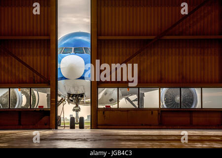 Blue airplane in front of half opened door to hangar Stock Photo