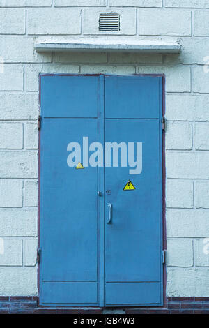 Photo texture of an old metal door on a wall of concrete bricks. Doors for electrical switchboard are painted in blue. High voltage sign Stock Photo