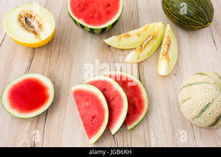 Arrangement of a variety of whole, halved and sliced melons on light brown wooden background. Stock Photo