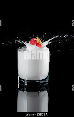 Strawberries fall into milk, splash, splashes on a black background. Stock Photo