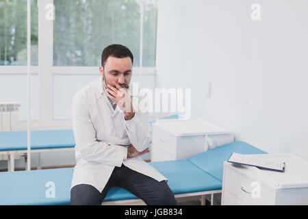 Thoughtful doctor sitting in a operating room with his hand on head Stock Photo