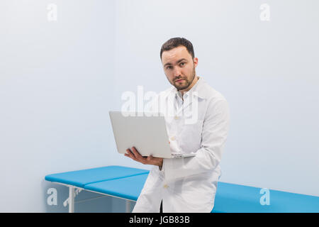 Portrait of cheerful doctor sitting at the desk working on laptop Stock Photo