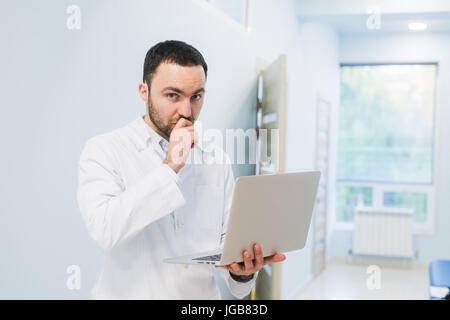 Minded successful doctor standing at his office and using laptop for his work Stock Photo