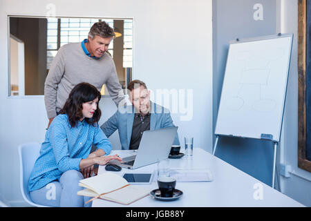 Focused office colleagues talking together while using a laptop  Stock Photo