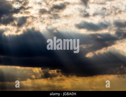 Beautiful sun shafts light coming through large and dark clouds, with a deep blue sky in contrast Stock Photo